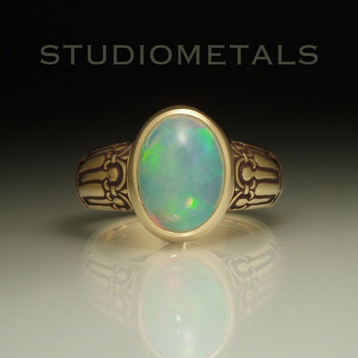 Large, oval crystal opal bezel set in a hand carved 18 karat yellow gold ring.