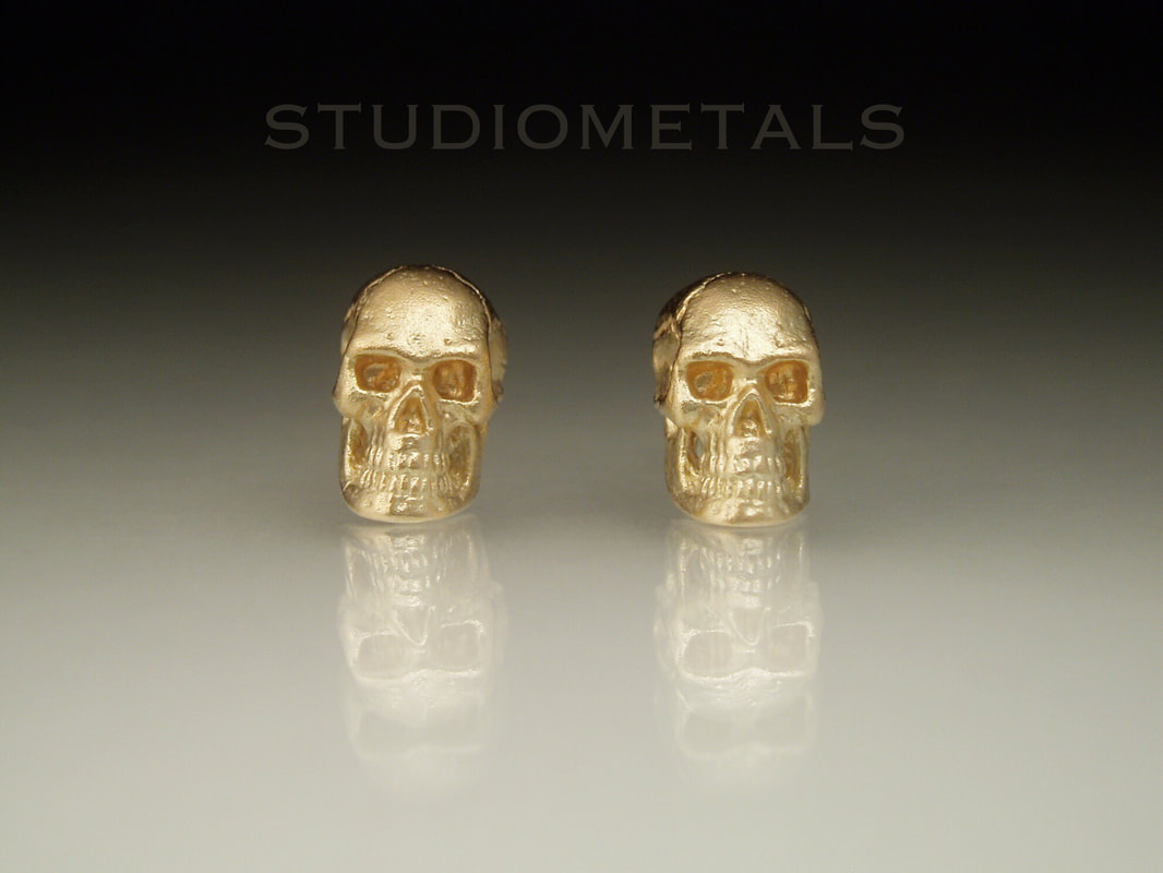 Solid 14 karat yellow gold human skull earrings with a matter finish.