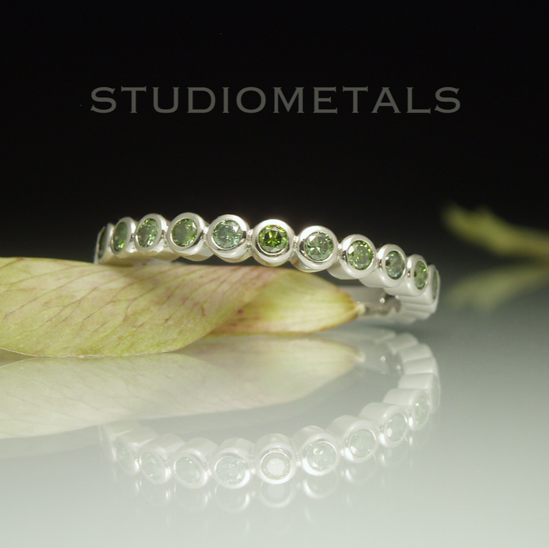 Bezel set green diamond bubble eternity band in 19k white gold.