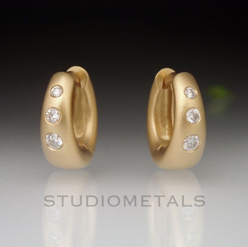 Wide tapered oval huggie hoop earrings in matte 18 karat yellow gold flush set with vvs diamonds.