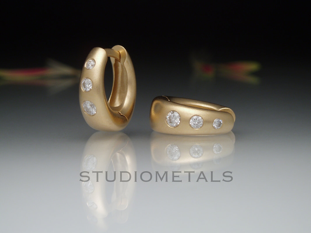 wide tapered oval huggies in matte gold with flush diamonds