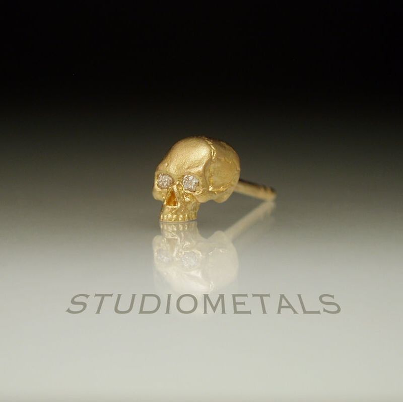 Single, jawless half skull stud earring in matte 18k yellow gold with diamond eyes.