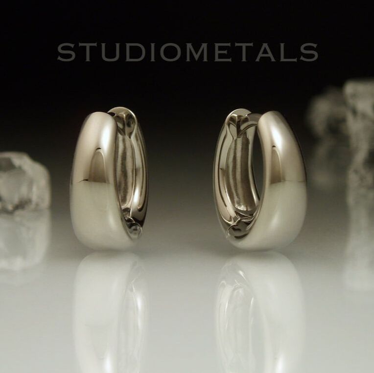 Wide, tepered, oval huggie hoop earrings in polished 19k white gold.